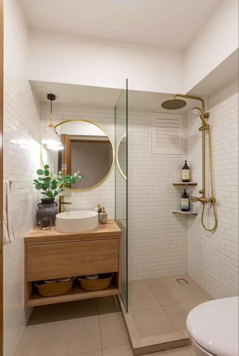 Petite salle de bain blanche et bois avec miroir rond. Robinetterie encastrée dorée. Paniers posés au sol